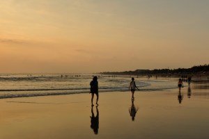 People walk along Kuta beach at sunset