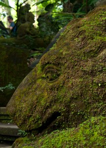 A lion statue lies in wait covered in moss in Ubud's Monkey Forest in Bali